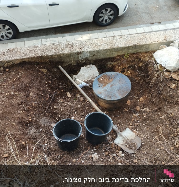 את חפירה ודלי ליד מכסה ביוב באדמה